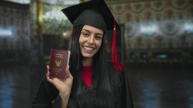 Mezuniyet şapkalı bir kadın elinde Tayland pasaportu ile evde gülümsüyor, bir müze dekorasyonunda seyahat etmeyi ya da öğrenim görmeyi öneriyor..