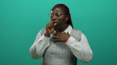 Örgülü, yeşil arka planda öksüren ve göğsünü tutarak parlak bir stüdyo ortamında endişe ya da sağlık sorunları öneren düşünceli bir kadın..