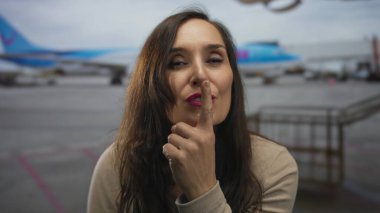 Havaalanı terminalinde sessiz kalmak için genç İspanyol kadın parmaklarını dudaklarına uzatıyor..
