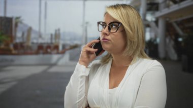 Gözlük takan kadın, şehirdeki hareketli caddede kollarını kavuşturarak akıllı telefonu kulağına tutuyor..