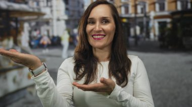 Gündüz vakti kalabalık bir şehirde, arka planda binalar olan hareketli bir şehirde elleri kalabalık bir şekilde el kol hareketi yapan kadın..