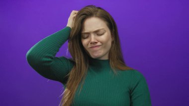 Baş ağrısı için el şakağına bastırılmış katı mor bir stüdyo duvarına kafa tutan kadın..