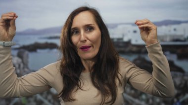 Genç İspanyol kadın, okyanusa tepeden bakan deniz kenarında el hareketleriyle konuşuyor. İletişim tutkusu..