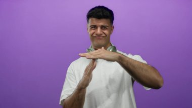 Beyaz tişörtlü genç İspanyol adam, kulaklıklarla mor duvar arkasına işaret veriyor..