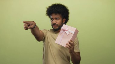 Elinde pembe hediye kutusu olan adam izole edilmiş sarı arkaplanı göstererek modern ve minimalist bir ortamda odaklanmış bir ifade aktarıyor..