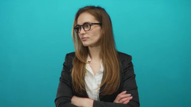 Stüdyoda kollarını kavuşturmuş gözlük takan beyaz bir kadın..