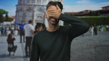 İspanyol asıllı genç adam, dışarıdaki pisa binasının tarihi eğimli kulesinin önünde poz veriyor..