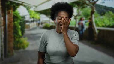 Arka planda yeşillik olan bir şehir caddesinde el ele gülen bir kadın samimi bir neşe anı yakalıyor..