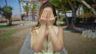 Kadın çerçeveleri elleri ile yüz ve gözleri kapalı gülücükler ağaçlar arasında güneş ışığı parkı yürüyüş yolu; neşe.