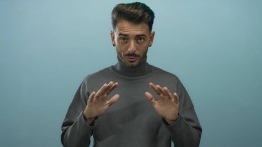 Genç İspanyol adam avuçlarını mavi stüdyoda tutuyor. Odaklanmış bakışlarla nazik bir duruş hareketi yapıyor. Huzur..