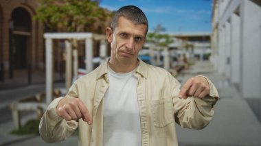 Beyaz binalar ve arka planda yeşillik ile güneşli bir sokakta aşağı doğru hareket eden beyaz bir adam kent ortamında yön vurgusunu iletiyor..