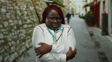 Steteskoplu bir kadın soğuk algınlığından titreyen, gözlüklü ve beyaz ceketli, şehir manzarası ile çevrili, soğuk bir hava veriyor..