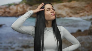 Deniz kenarında düşünceli bir kadın, beyaz elbiseli İspanyol kadın deniz kenarında duruyor, derin düşüncelere dalmış bir ifadeyle, sakin sahil ve suyla çevrili..