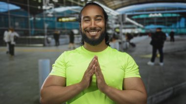Elleri havada gülümseyen bir adam çıplak kollarını ve kaslı duruşunu gösteren işaret levhasında yoğun havaalanı terminalinde neon yeşil tişörtle; farkındalık.