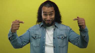 Sakallı, kot ceketli ve beyaz tişörtlü adam göğüs göğse, limon yeşili bir stüdyoda gülümsüyor..