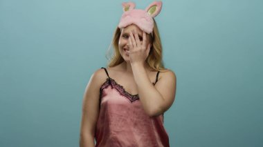 Pembe gecelikli bir kadın mavi bir arka planda tavşan gözlü bir maskeyle gülümsüyor, neşeli ve neşeli bir gece ortamı yaratıyor..