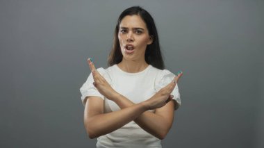 Gri stüdyoda, çatık kaşlı, aralıklı dudaklı ve doğrudan bakışlı kadın ellerini sıkıca çaprazlar..