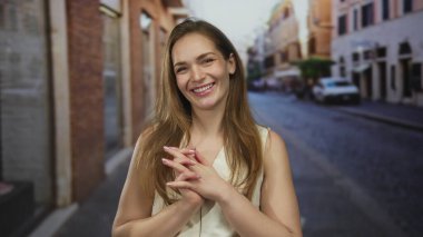 Kalabalık bir şehir sokağındaki tuğla binaların önünde sırıtan genç bir kadın. Mutluluk..