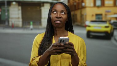 Akıllı telefondan mesajlaşan kadın, şehir caddesinde dikilip duygusal ifadeler sergilemekten ve şehir geçmişini soyutlamaktan bıkmış gibi görünüyor..