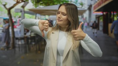 Şehir caddesindeki terasta, açık kahve dükkanının ambiyansıyla çevrili karışık duyguları olan bir kadın..