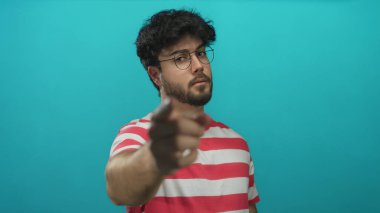 Sakallı ve gözlüklü genç İspanyol adam mavi arka plana karşı parmak işareti yaparak buraya gelir..