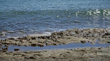 Akdeniz dalgaları güneşli bir günde kayalık kıyılara nazikçe yaklaşarak açık deniz manzarasını renklendirir..
