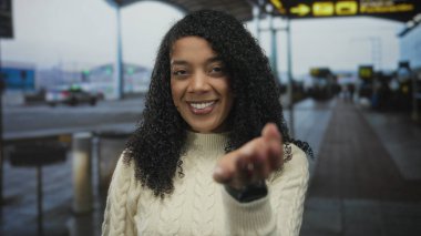 Krem rengi kazak giyen kadın avucunu yukarı uzatıyor ve yoğun havaalanı terminalinde gülümsüyor; sıcak konukseverlik.