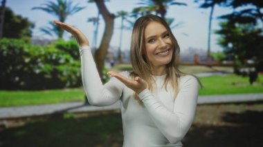 Genç sarışın kadın, güneşli bir açık havada canlı ağaçlarla çevrili yemyeşil bir parkta neşeli ve kaygısız bir atmosfer sergiliyor..