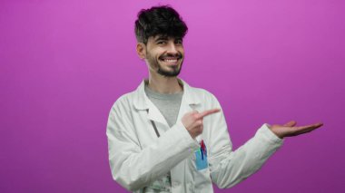 Laboratuvar önlüğüyle gülümseyen bir adam pembe arka plana el uzatıyor. Cebinde kalemler ve kimlik kartı var. Profesyonel ya da bilimsel bir ortam öneriyor..
