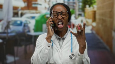 Açık terasta akıllı telefondan konuşan, steteskoplu beyaz önlük giyen bir kadın kalabalık cadde ve kahve dükkanı ortamının ortasına odaklanmış görünüyor..