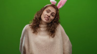 Tavşan kulaklı, yeşil arka planda sırıtan kıvırcık saçlı, rahat bir kazak giyen, neşeli bir kutlama ve neşeli bir ortam için izole edilmiş bir kadın..