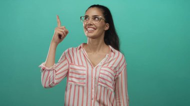 Gözlüklü İspanyol kadın yeşil stüdyo duvarının önünde yukarı doğru işaret ediyor; ilham verici iyimserlik.