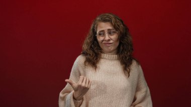 Kırmızı arka planda, gözlük ve süveter takan, isteksizlik ya da belirsizlik hissini aktaran, kuşkularını dile getiren bir kadın..