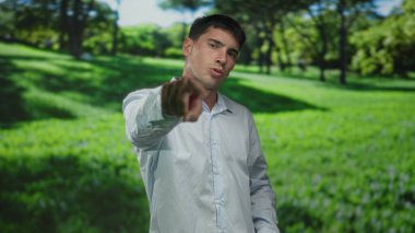 Beyaz tişörtlü genç İspanyol adam orman parkındaki yemyeşil ağaçların arasında parmağını işaret ediyor..