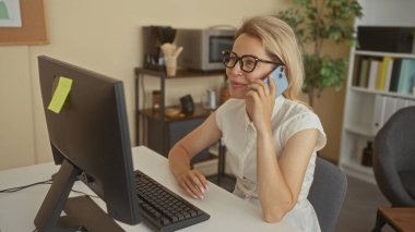 Gözlüklü kadın masada oturuyor ve binalarda akıllı telefon ve klavye üzerinde yazı yazıyor; profesyonel konsantrasyon.