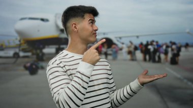 Havaalanındaki Latin asıllı genç adam hava alanının arka planında rahatlamış seyahat anını gösteren jestler yapıyor.
