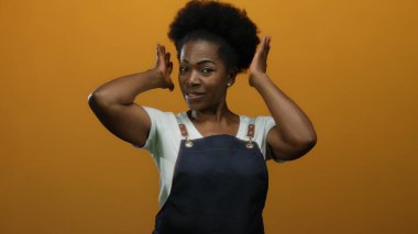 İzole edilmiş turuncu arka planda önlükle gülümseyen kadın neşe ve kendine güven gösteriyor.