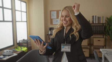 Modern ofis ortamında tablet kullanarak gülümseyen bir kadın. Kapalı mekan ışıklandırması, resmi bir iş elbisesi içinde mutluluk ve nişan gösterisi yapıyor..