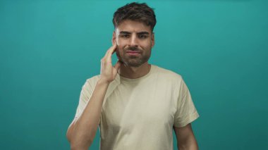 Stüdyo ortamında diş ağrısı için bej tişört giyen İspanyol genç adam..