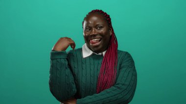 İzole edilmiş yeşil arka plana gülümseyen yeşil süveter giyen neşeli bir ifadeyle canlı pembe örgüler takan mutlu ve kendine güvenen bir kadın..