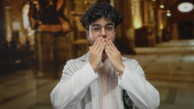 Kilisede sakallı ve gözlüklü genç bir adam öpüşüyor, beyaz bir ceket giyiyor, ev kemerleriyle çevrili ve sakin ve düşünceli bir atmosfer için sıcak bir ışık..