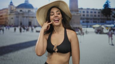 Hasır şapka ve bikinili kadın, Vatikan meydanında güneş ışığı altında çıplak omuzlu çağrı jesti yapıyor; bağlantı neşesi.