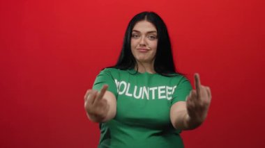 Yeşil gömlekli bir kadın, kırmızı arka planda saygısız davranışlar sergiliyor tutumunu ve kendine güvenini oyuncu bir ifadeyle ifade ediyor..