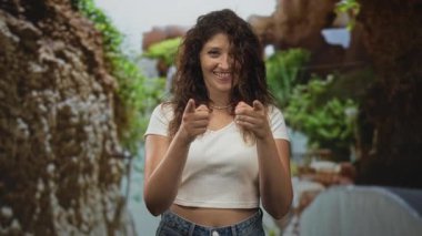 Yeşil yapraklı, gülümseyen ve göz kırpan orman parkında beyaz tarladaki kadın kameraya iki parmağını da gösteriyor..