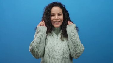 Canlı mavi arka planda, rahat süveter giyen bir kadın stüdyo ortamında izole edilmiş mutluluğu ifade ediyor.
