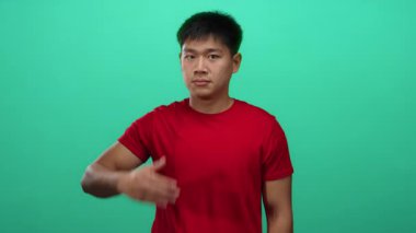 Kırmızı tişörtlü genç adam yeşil arka plan duvarına karşı yüzünü kapatıyor. Duygularını ve mahremiyetini canlı ve anlamlı bir şekilde ifade ediyor..