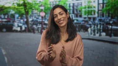 Kanal kenarında el çırpan bir kadın, pembe bir kazak içinde gülümsüyor; nazikçe memnuniyet.