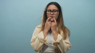 Stüdyoda elleri ağızda tırnak yiyen bir kadın, soluk mavi bir fon karşısında gözlük ve yüzükler takıyor; endişeli mavi.