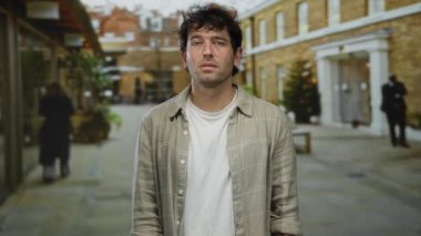 Açık havada gömlekli bir adam şehir caddesinde gözleri kapalı duruyor. Tuğla binalar ve Noel süslemeleri ile modern bir şehrin arka planına karşı duygularını gösteriyor..