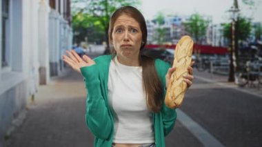 Bisiklet ve kanalın yakınındaki işlek bir caddede düşünmek için elleri çenesinde uzun bir baget tutan kadın; belirsizlik.